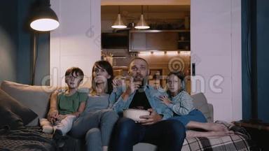 快乐微笑的年轻白种人母亲，父亲和两个孩子一起在家里的沙发上看电影，使用在线电影。